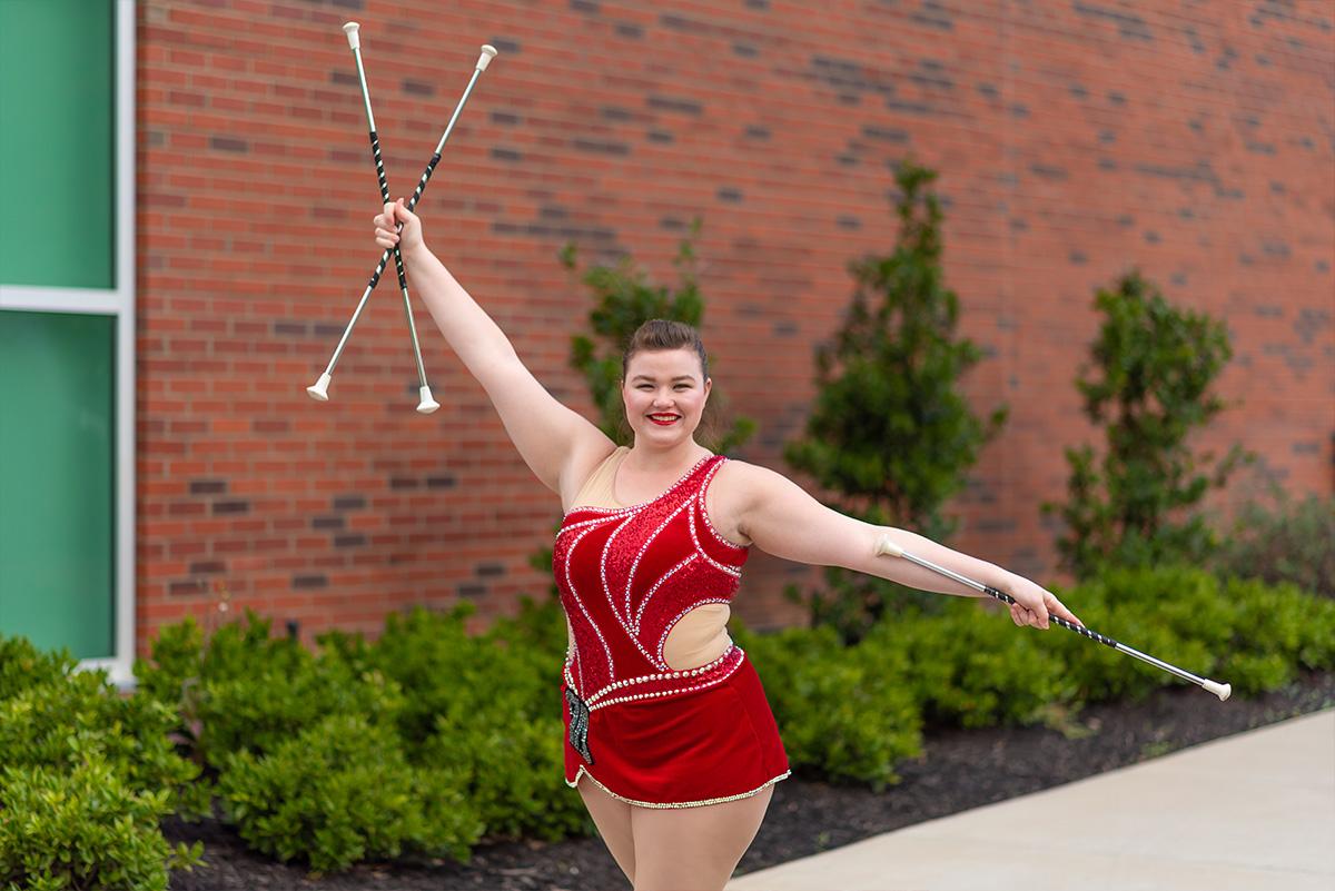 Izzy Melvin poses in front of Art and Design building with twirling batons